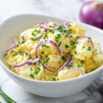 Schwäbischer Kartoffelsalat mit Zwiebeln und Schnittlauch in weißer Schale auf Marmortisch
