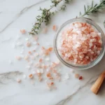 Feines rosa Salz in einer Glasschale auf Marmor mit Kräutern