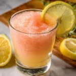 A glass of refreshing pink detox water with lemon and pink Himalayan salt, garnished with a lemon slice and surrounded by fresh lemon slices.