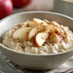Nahaufnahme von Haferbrei mit Apfelscheiben und Zimt auf rustikalem Frühstückstisch